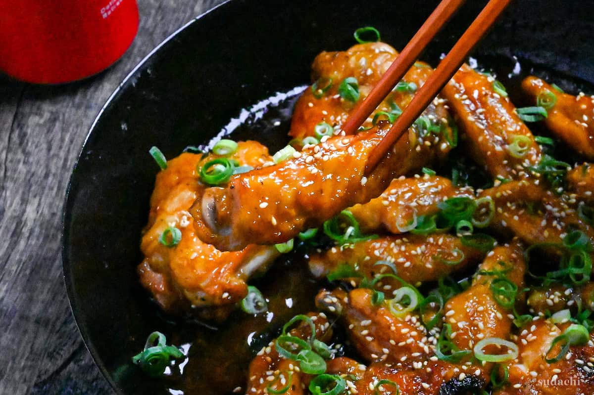 Mock teriyaki made with chicken wings in a black pan sprinkled with green onions and sesame seeds