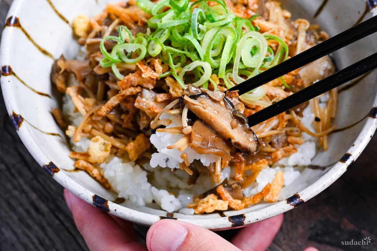 black chopsticks holding mushrooms and rice over a bowl of kinoko donburi