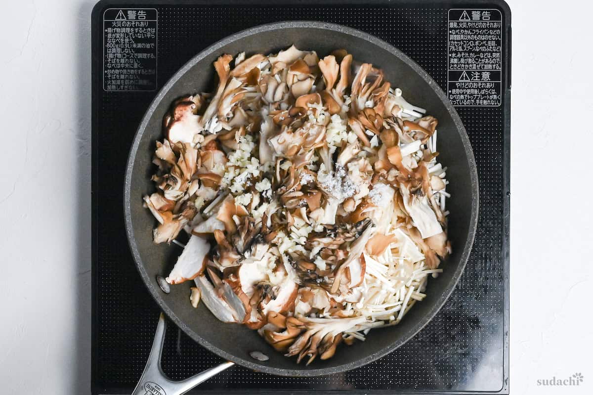 shiitake, enoki and maitake mushrooms frying in a pan with garlic, salt and oil