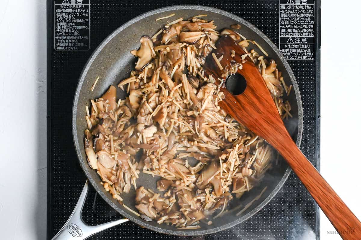 fried mushrooms in sauce in a frying pan on the stove top with wooden spatula