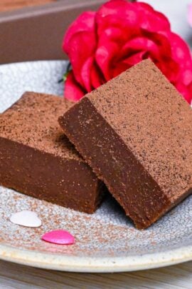 2 pieces of nama chocolate stacked on a plate with an imitation rose and a gift box of nama choco in the background