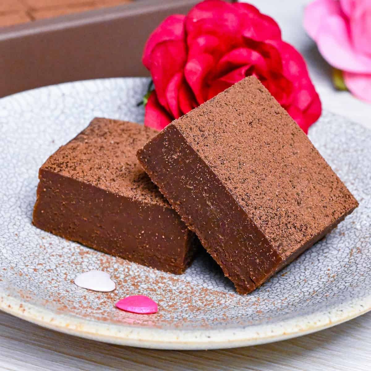2 pieces of nama chocolate stacked on a plate with an imitation rose and a gift box of nama choco in the background