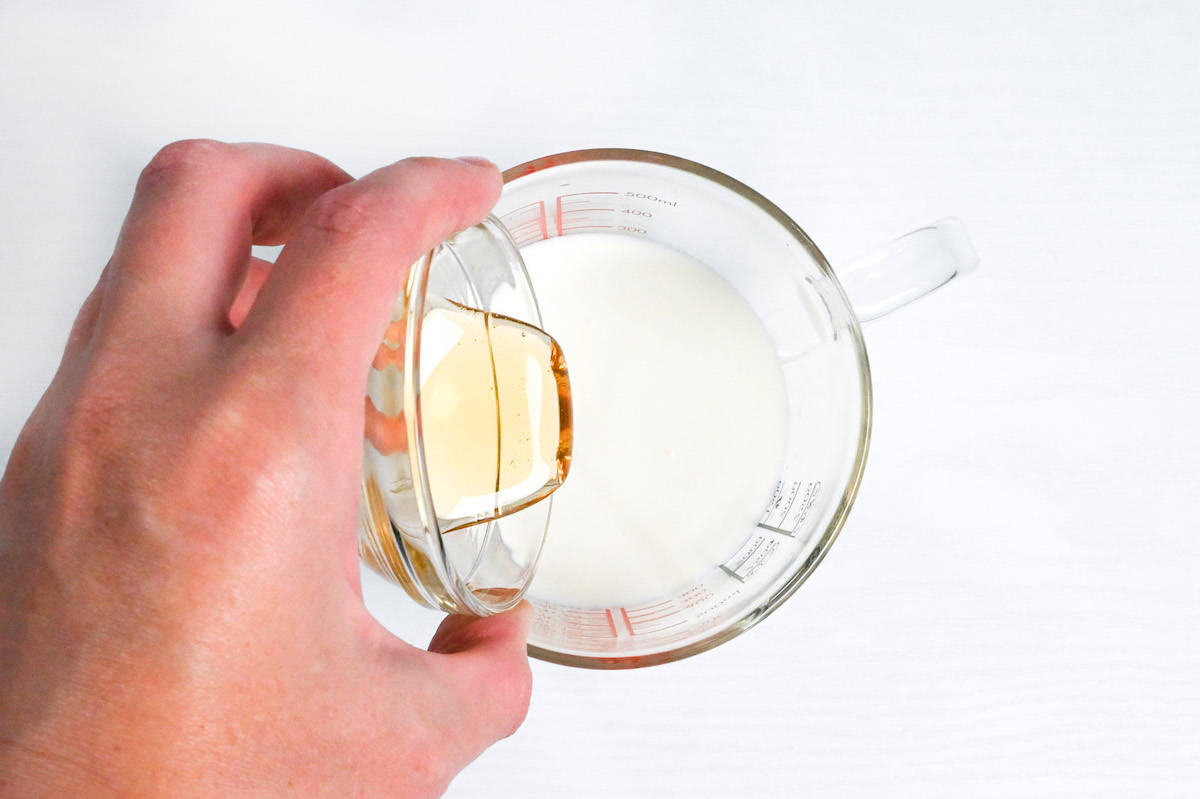 pouring honey into a glass jug with water and cream inside