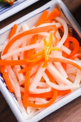 Kohaku namasu made with daikon and carrot served in a square white dish topped with yuzu peel