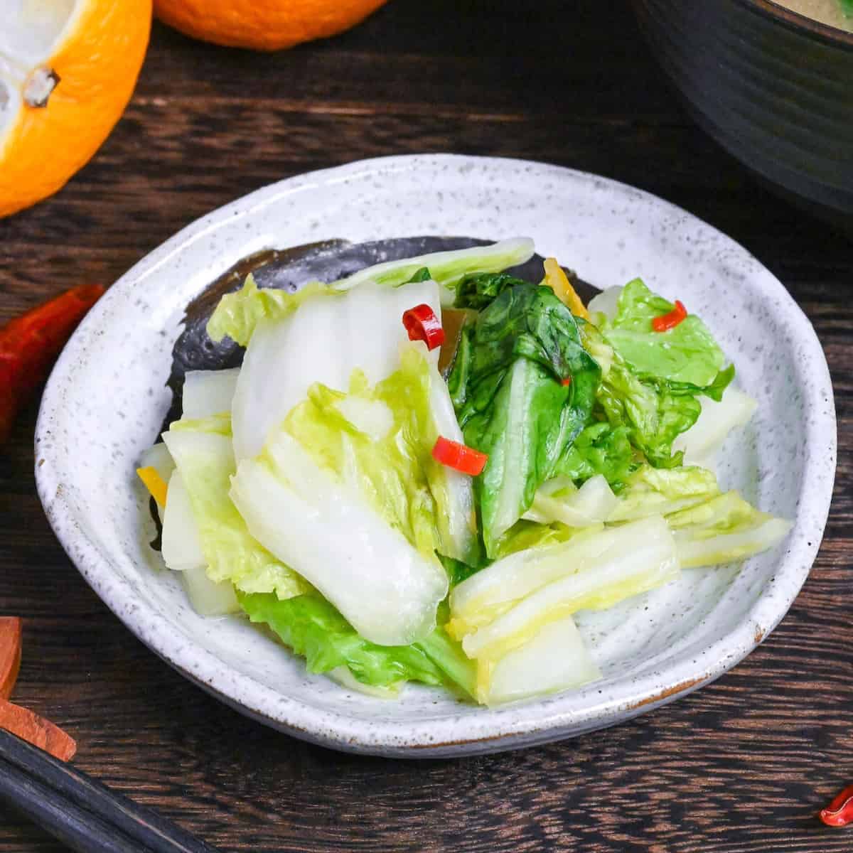 Japanese Napa Cabbage Pickles (Hakusai No Asazuke) on a small white plate with brown brushstroke design next to yuzu citrus and a bowl of miso soup