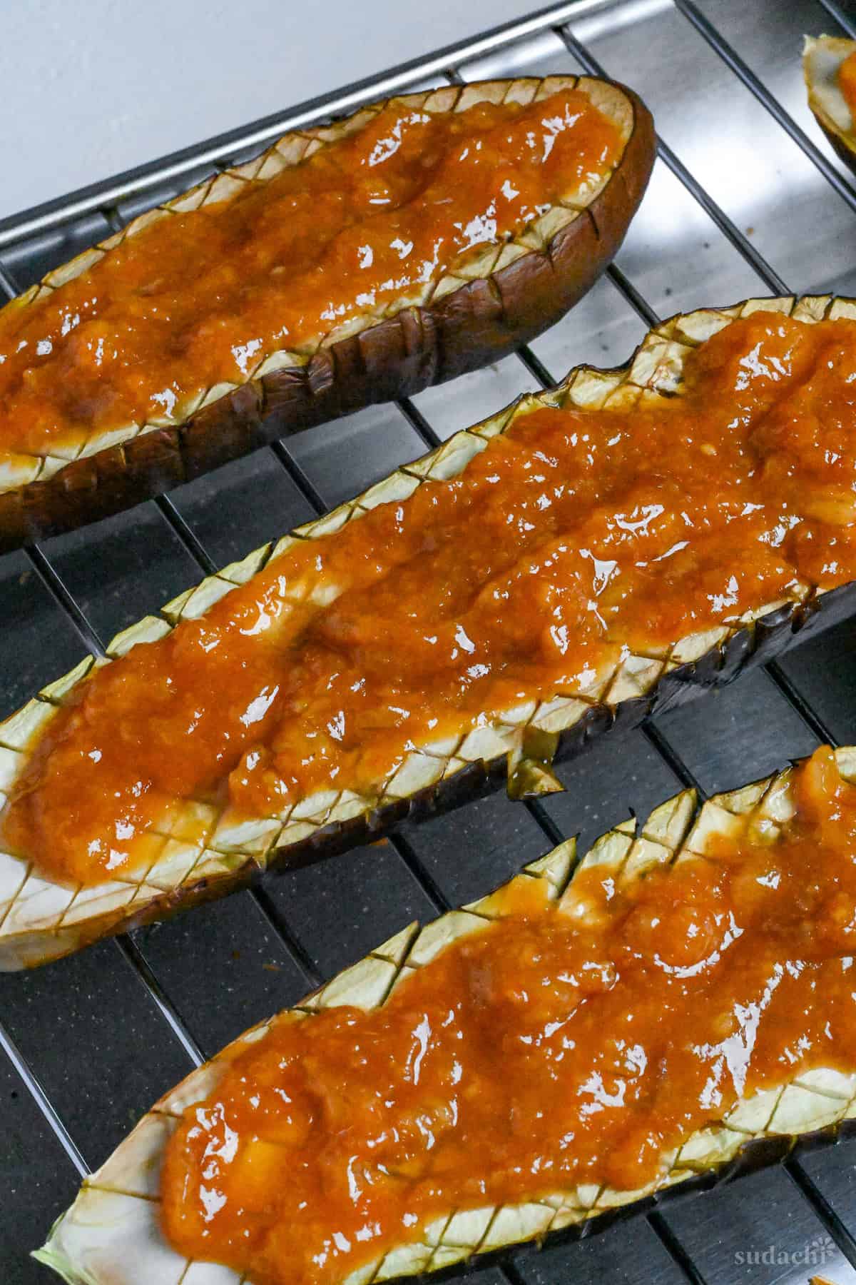 Scored eggplant halves topped with miso glaze on a wire rack ready for grilling