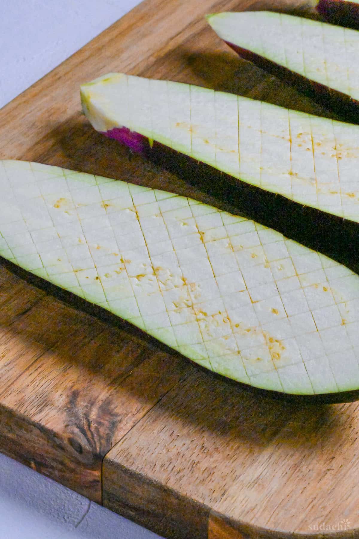 scored eggplant halves on a wooden chopping board