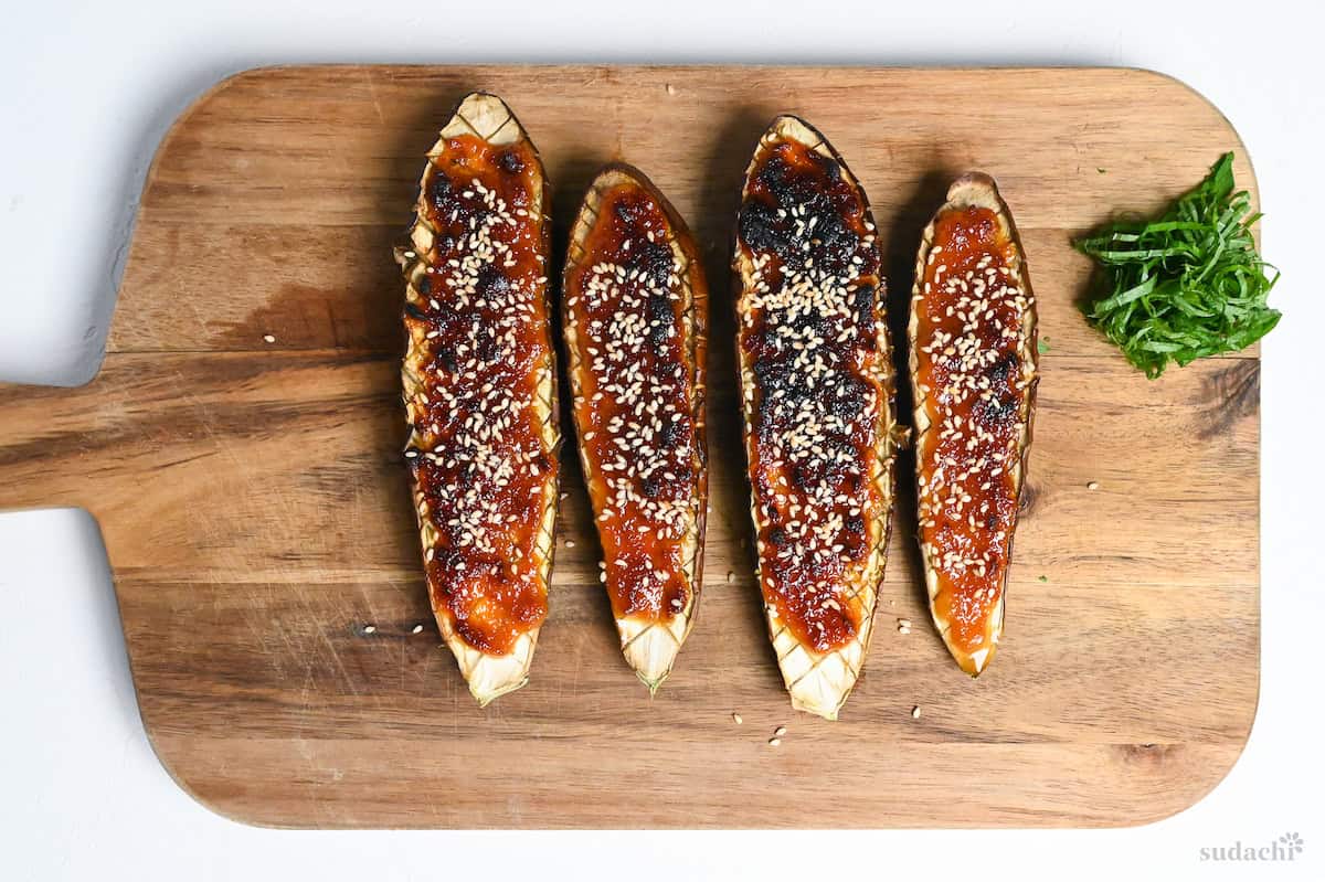 Miso glazed eggplants on a wooden chopping board topped with white sesame seeds