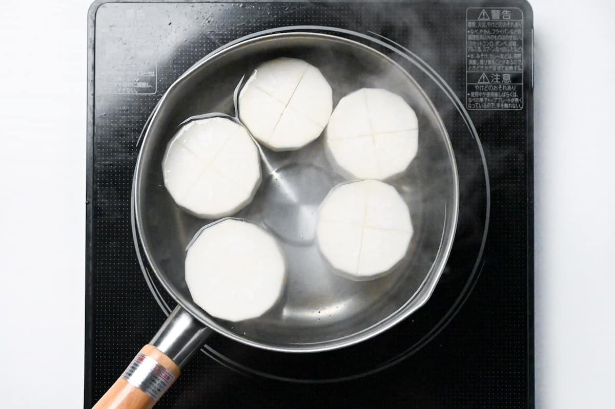 scored rounds of daikon radish simmering in a pot of water