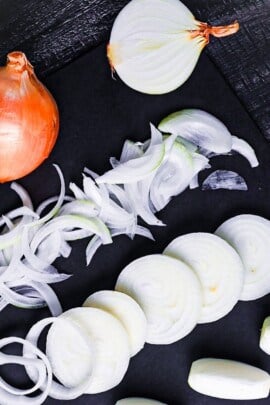 yellow onions cut in various ways on a black chopping board