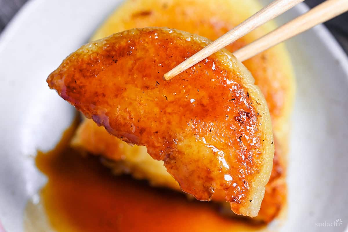 Half a potato mochi held up with light wooden chopsticks close up