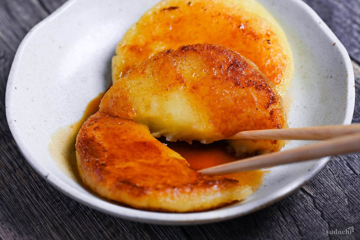 breaking one potato mochi in half with wooden chopsticks