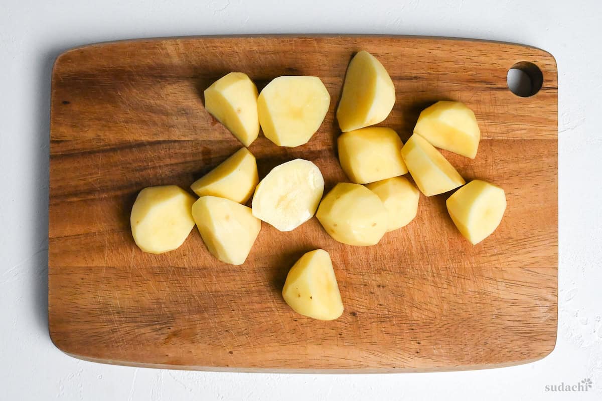 peeled potatoes cut into smaller pieces on a wooden cutting board