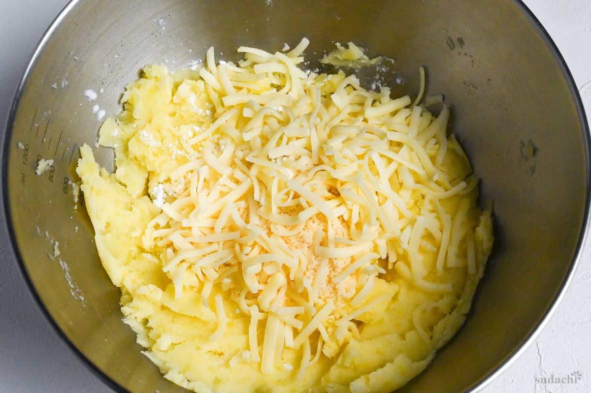 mashed potatoes in a steel mixing bowl with shredded cheese, powdered cheese and starch close up