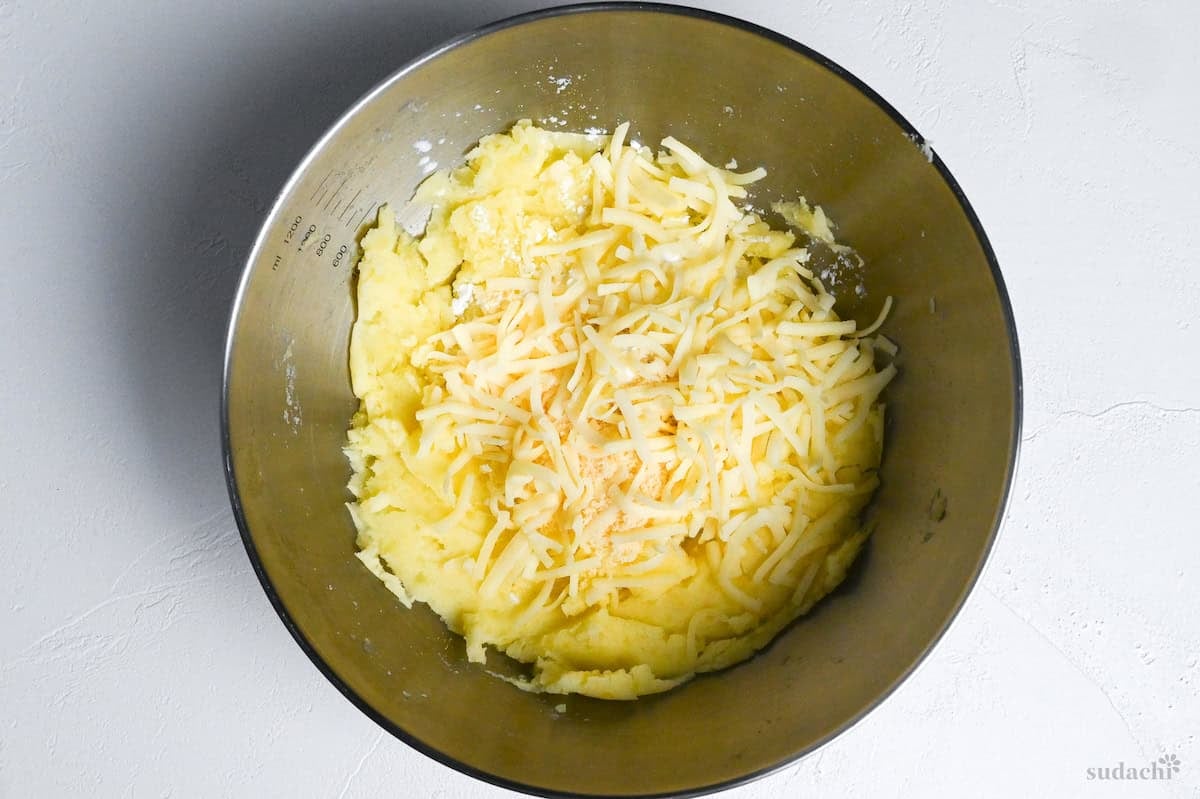 mashed potatoes in a steel mixing bowl with shredded cheese, powdered cheese and starch top down