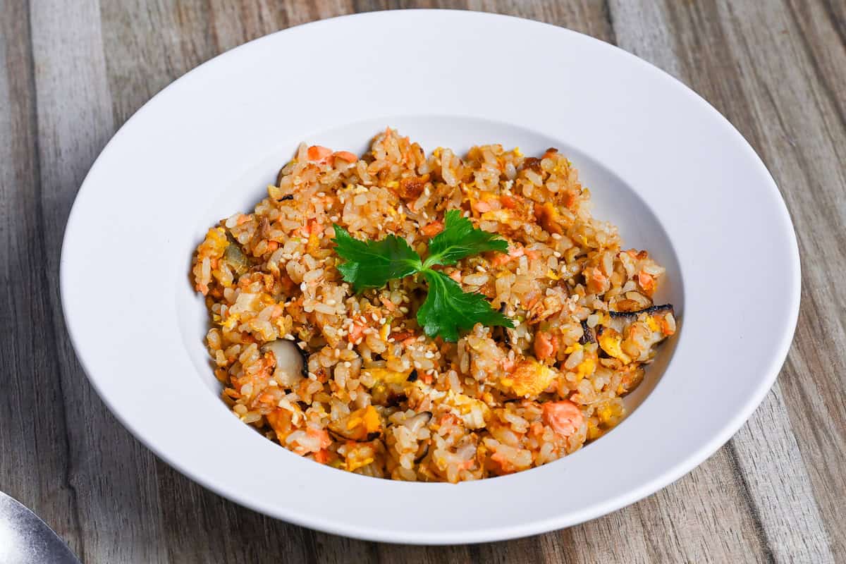 Salmon fried rice served in a white dish and garnished with mitsuba (Japanese wild parsley) side view
