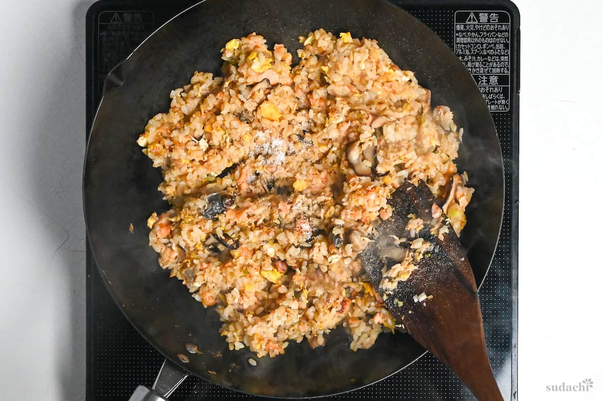 seasonings added to salmon fried rice in a wok on the stove