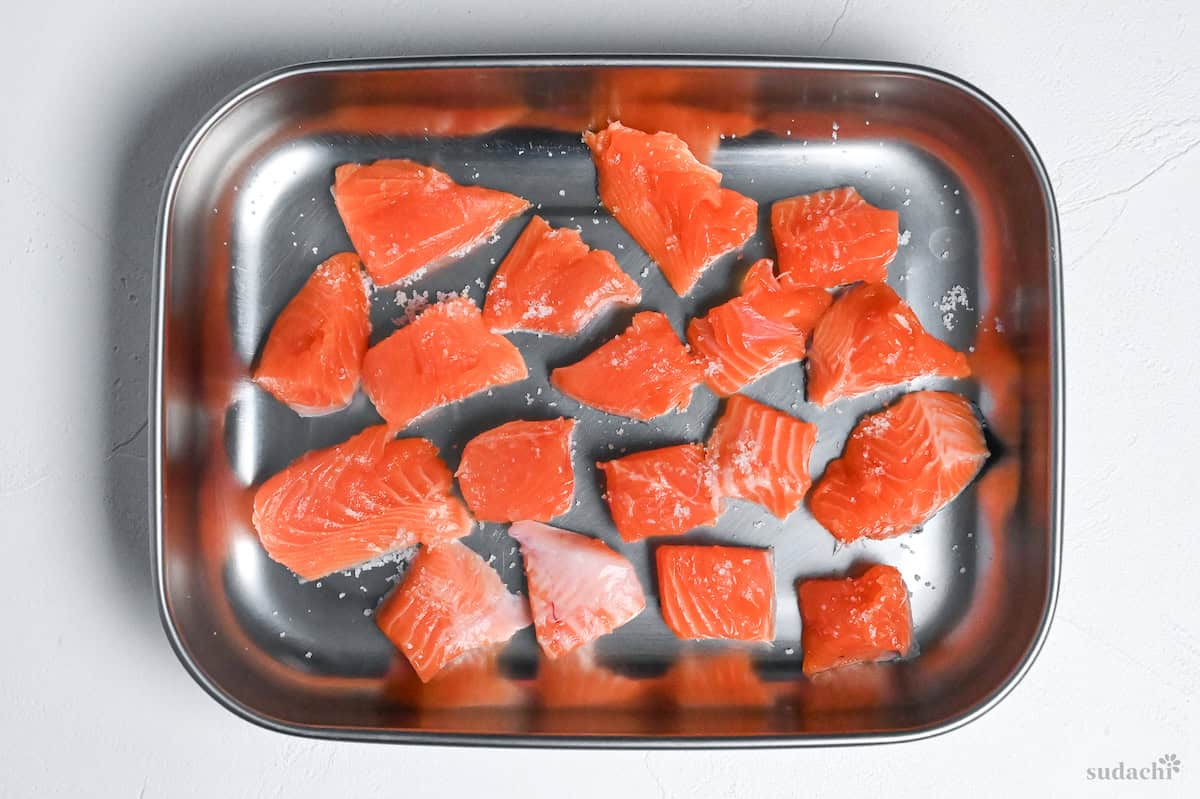 salmon pieces sprinkled with salt in a steel container on a white background