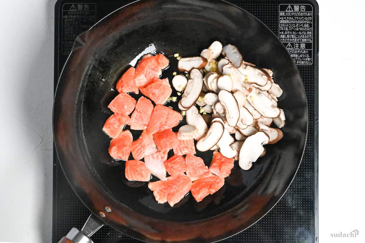salmon, mushrooms and ginger in a wok on the stove top