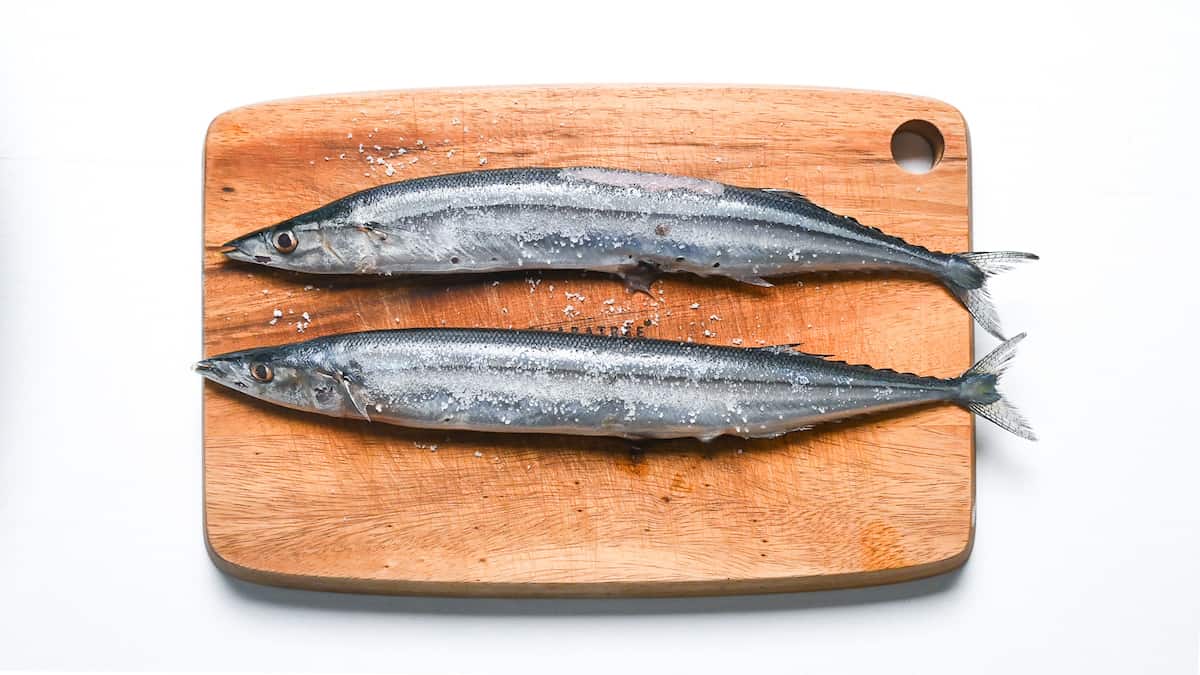 2 pacific saury sprinkled with salt on a wooden chopping board