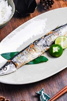 Grilled pacific saury (sanma no shioyaki) on a pale oval plate with grated daikon, sauce sauce and a halved sudachi