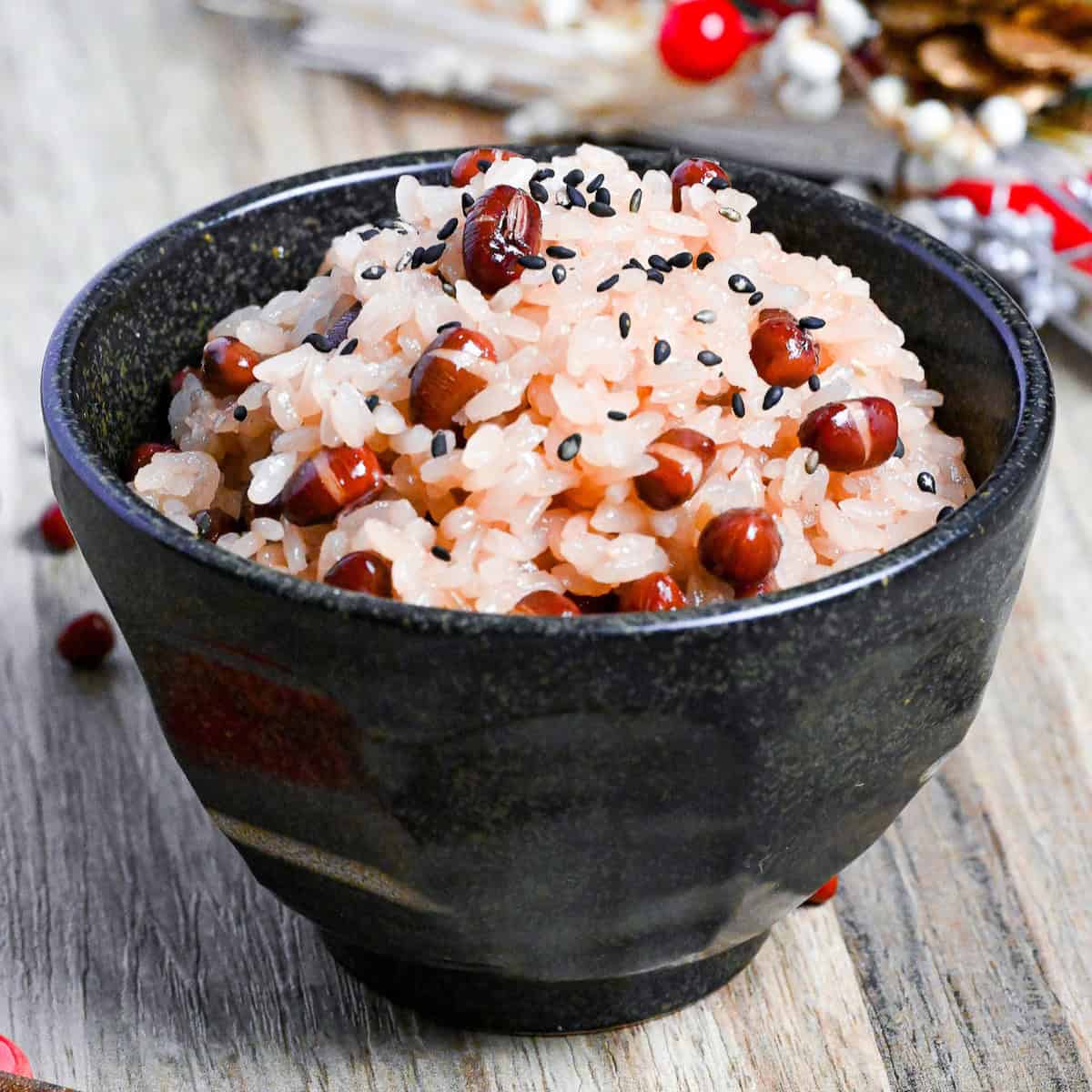 sekihan (red bean rice) in a black rice bowl sprinkled with coarse salt and black sesame seeds on a light wooden surface