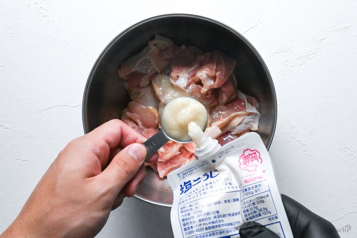pouring shio koji into a bowl with chicken thigh pieces