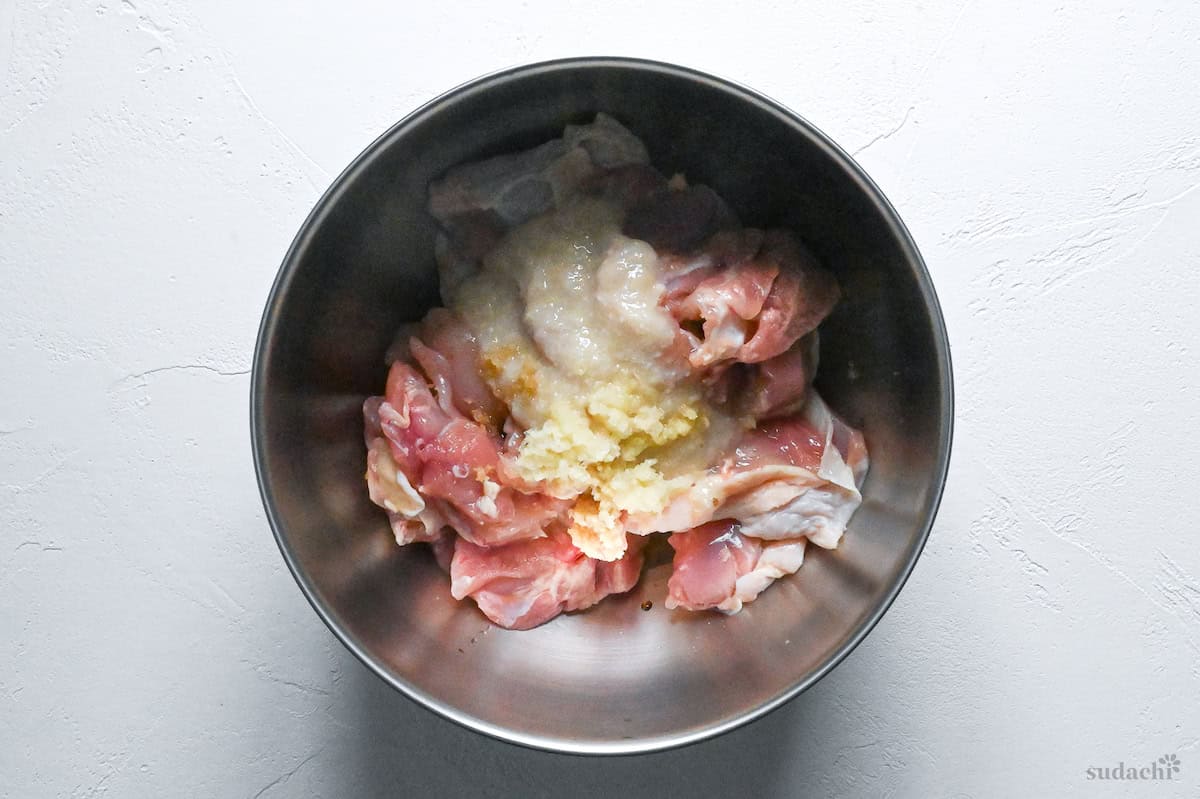 chicken thigh pieces in a bowl with shio koji, grated garlic, grated ginger, sake, light soy sauce before mixing