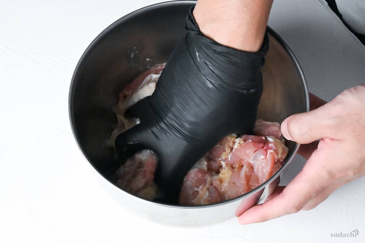 mixing shio koji marinade with chicken thigh pieces in a mixing bowl with a gloved hand