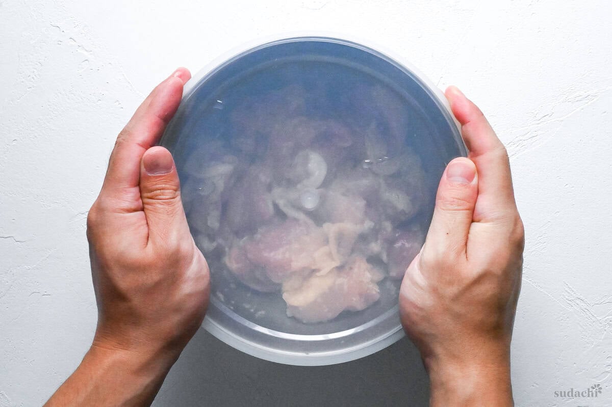 shio koji coated chicken thigh pieces in a metal mixing bowl with transparent silicone lid ready for refrigeration