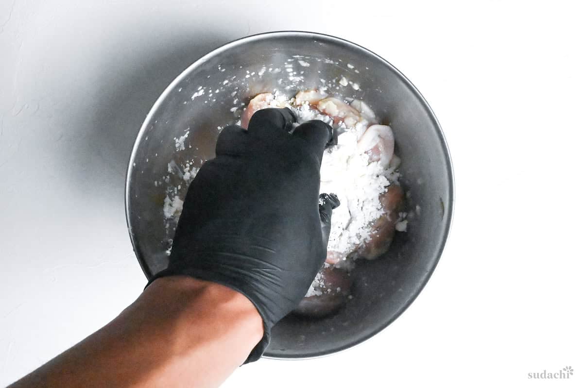 a hand mixing flour and starch into shio koji and chicken mixture