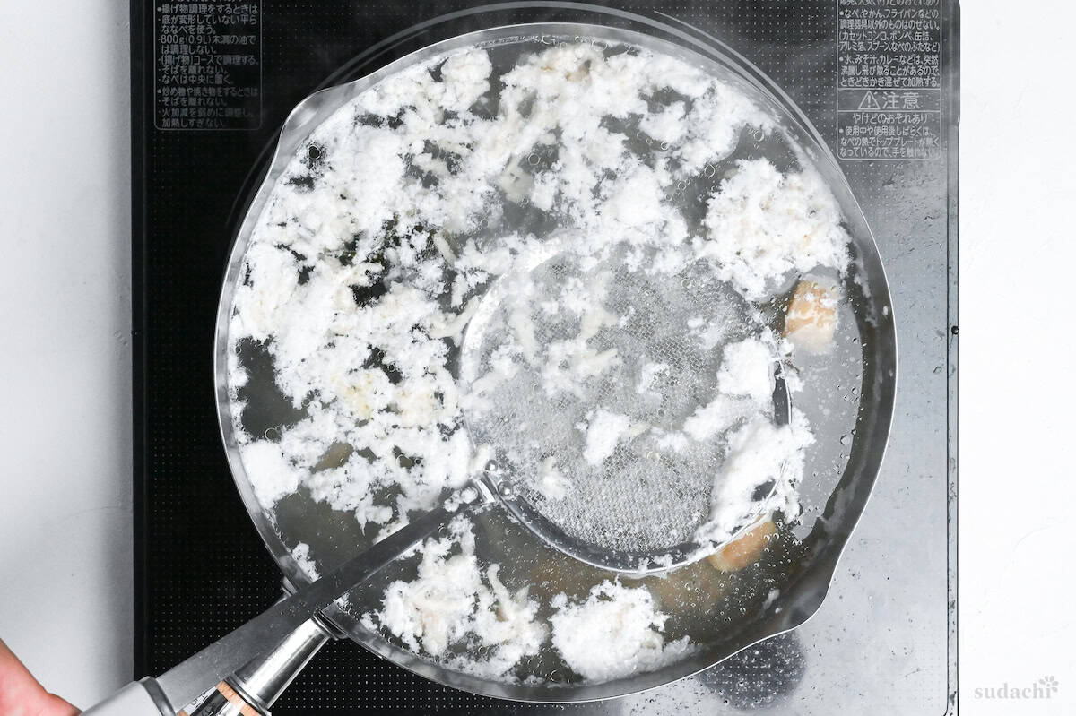 scooping scum out of shio ramen broth base using mesh spoon