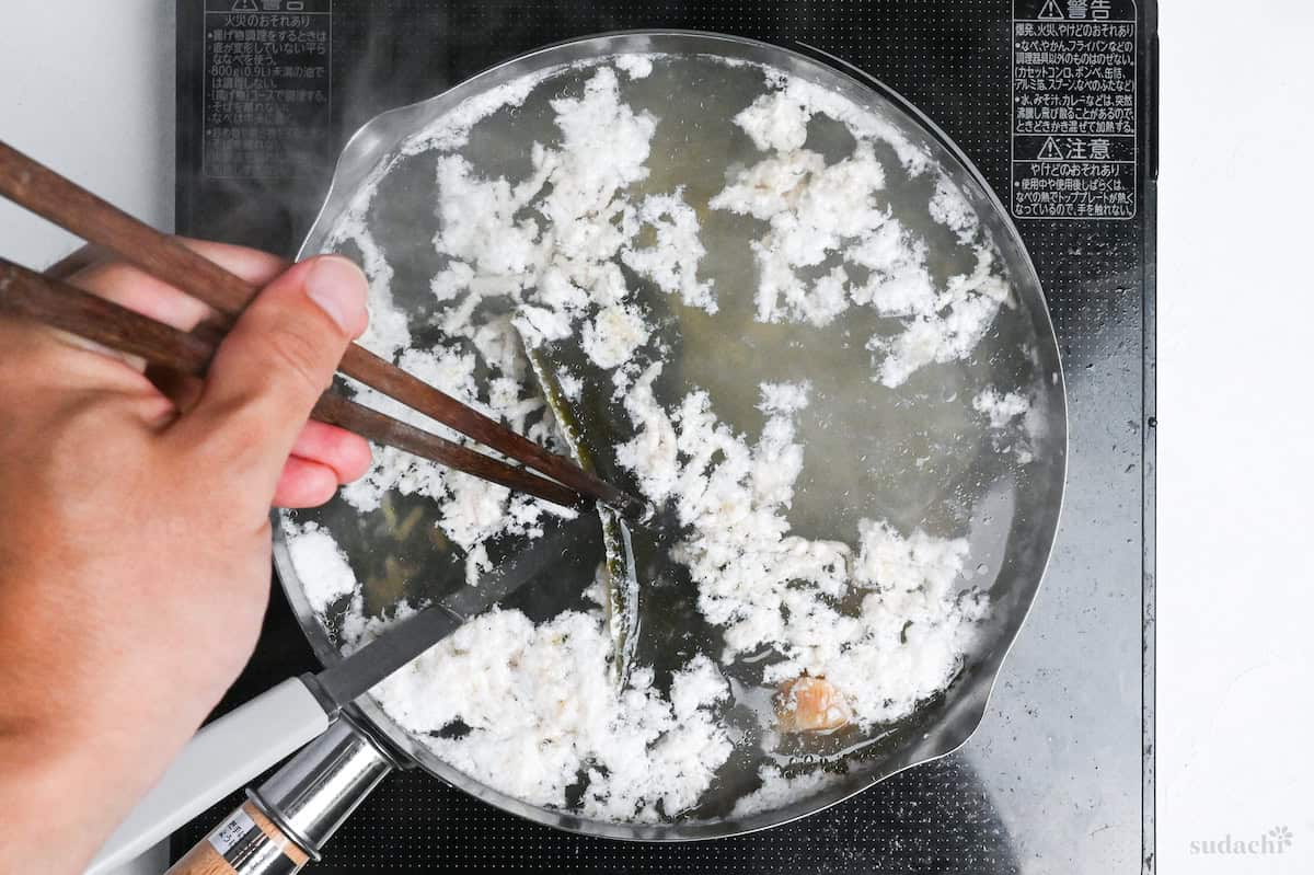 pulling kombu out of shio ramen broth with wooden cooking chopsticks