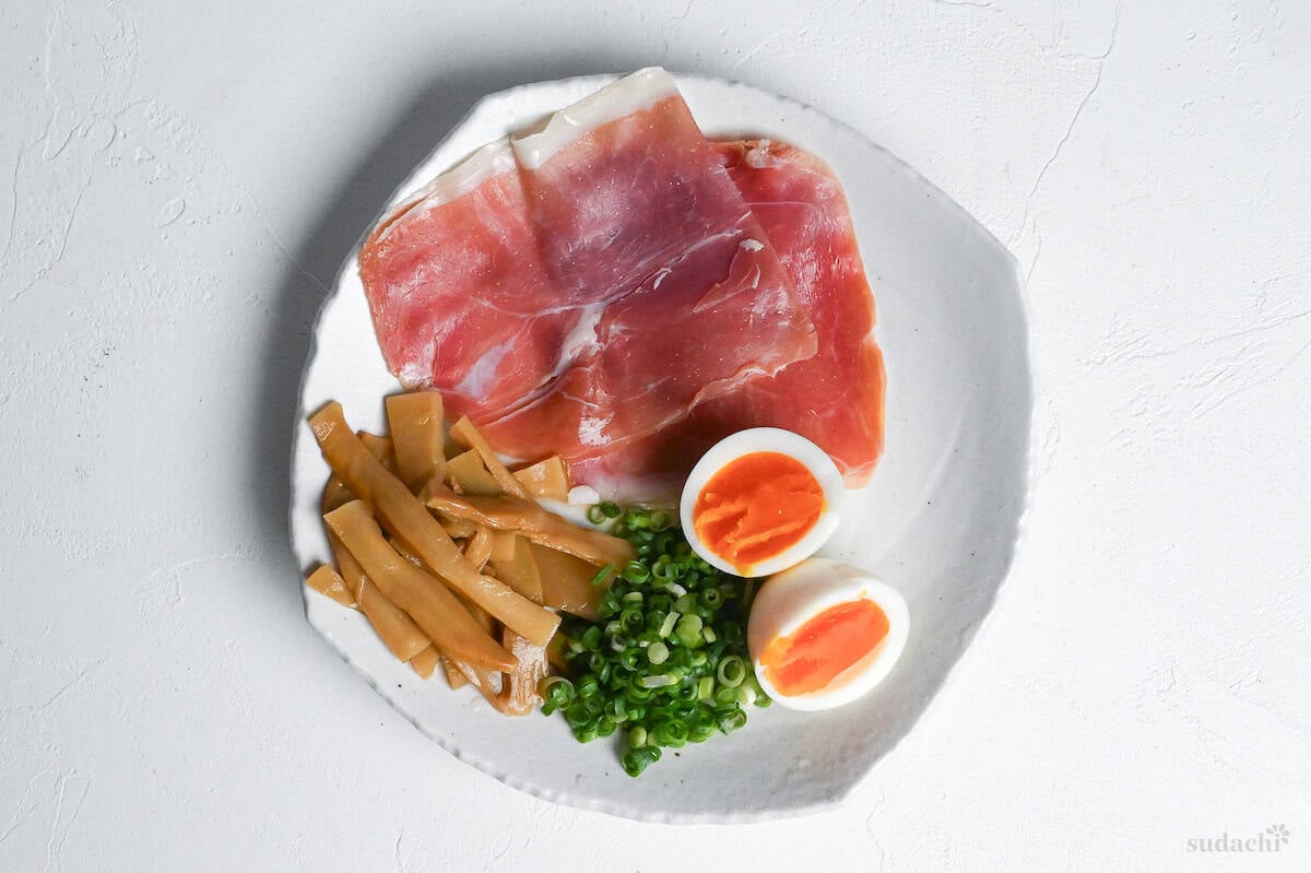 shio ramen topping ideas on a plate including cured ham, menma bamboo shoots, chopped green onion and soft boiled eggs