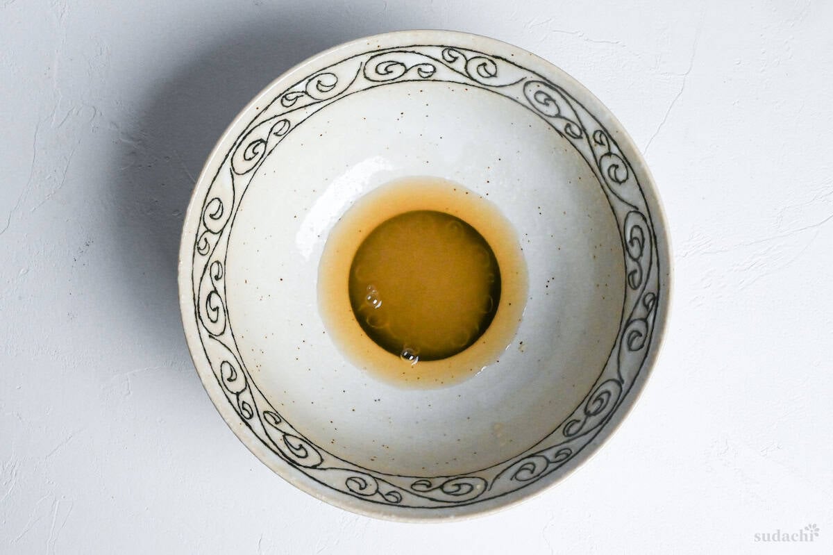 shio ramen tare (sauce base) in a cream bowl with black patterned rim