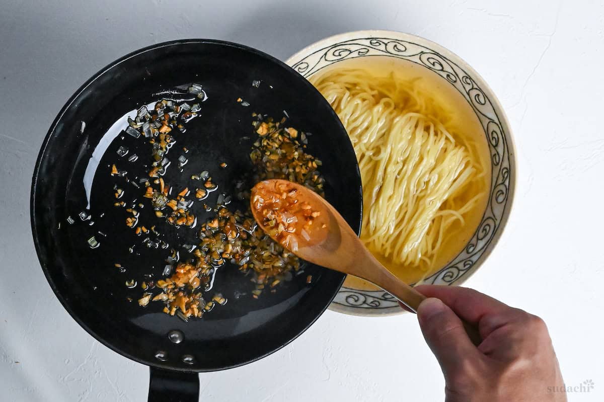 spooning crispy fried leeks over shio ramen in a bowl
