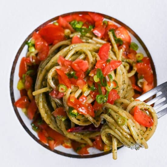 Japanese shiso pesto pasta topped with marinated tomato in a white pasta dish with silver fork top down