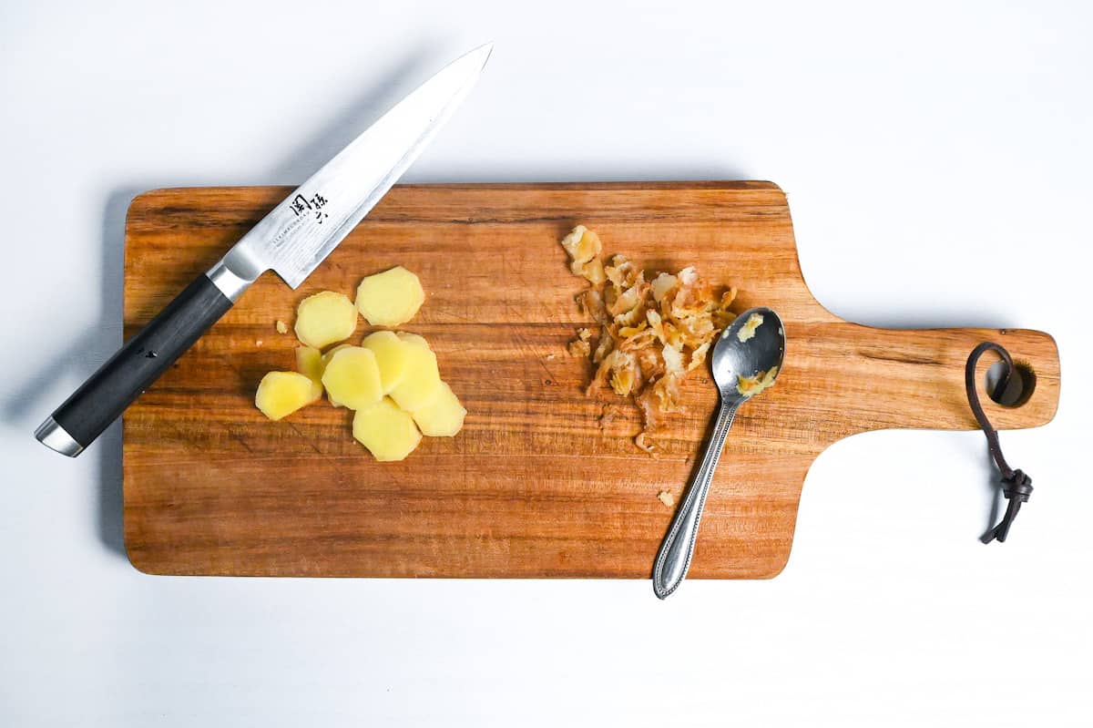 peeled ginger cut into thin slices on a wooden chopping board