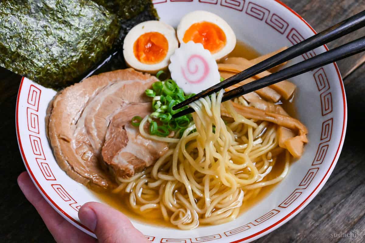 Black chopsticks lifting noodles from a bowl of homemade shoyu ramen