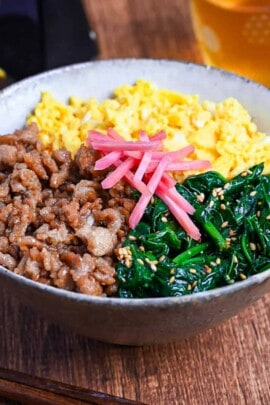 sanshoku don made with chicken soboro, scrambled egg and blanched spinach served over rice and topped with red pickled ginger on a wooden background