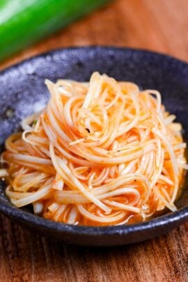 Spicy Negi (Strings of Japanese leek in a spicy dressing) in a black bowl on a wooden background