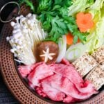 Traditional Japanese beef sukiyaki made with homemade sauce, thinly sliced wagyu beef, grilled tofu, shiitake mushrooms, enoki, carrots, napa cabbage, Japanese leeks and napa cabbage in a cast iron pot