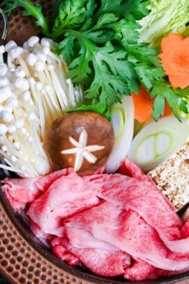 Traditional Japanese beef sukiyaki made with homemade sauce, thinly sliced wagyu beef, grilled tofu, shiitake mushrooms, enoki, carrots, napa cabbage, Japanese leeks and napa cabbage in a cast iron pot