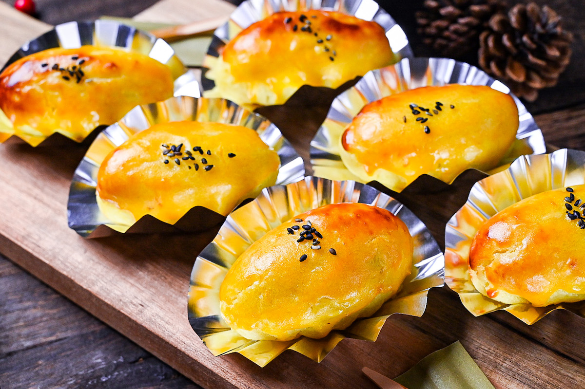 Japanese sweet potato dessert in foil cases sprinkled with black sesame seeds on a wooden chopping board