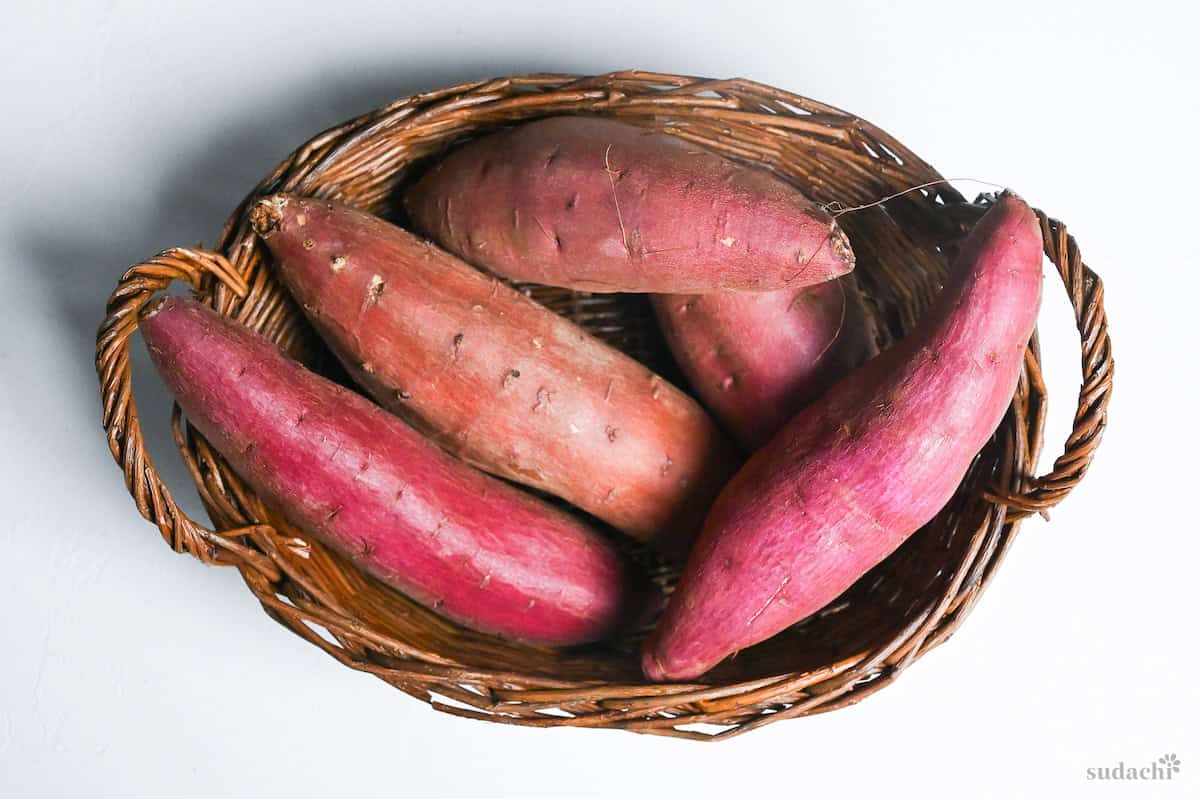 Different types of Japanese sweet potato in a woven basket on a white background
