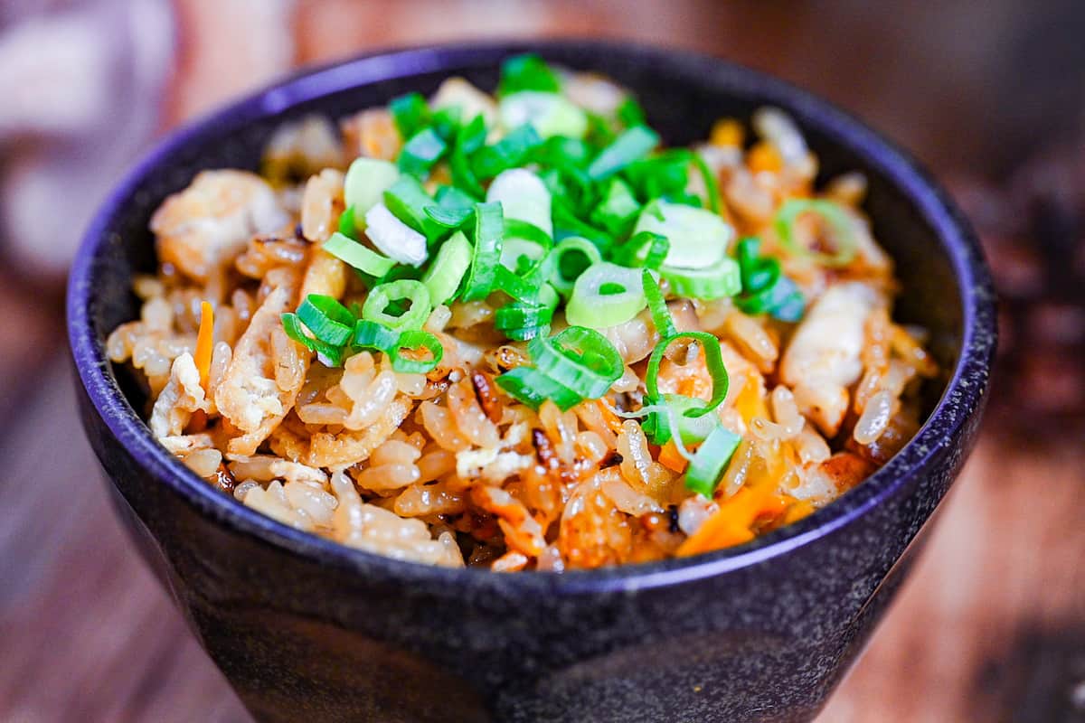 chicken takikomi gohan in a black rice bowl topped with chopped green onion