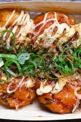 8 homemade takoyaki topped with takoyaki sauce, mayonnaise, bonito flakes, aonori and chopped green onions served in a bamboo boat top down