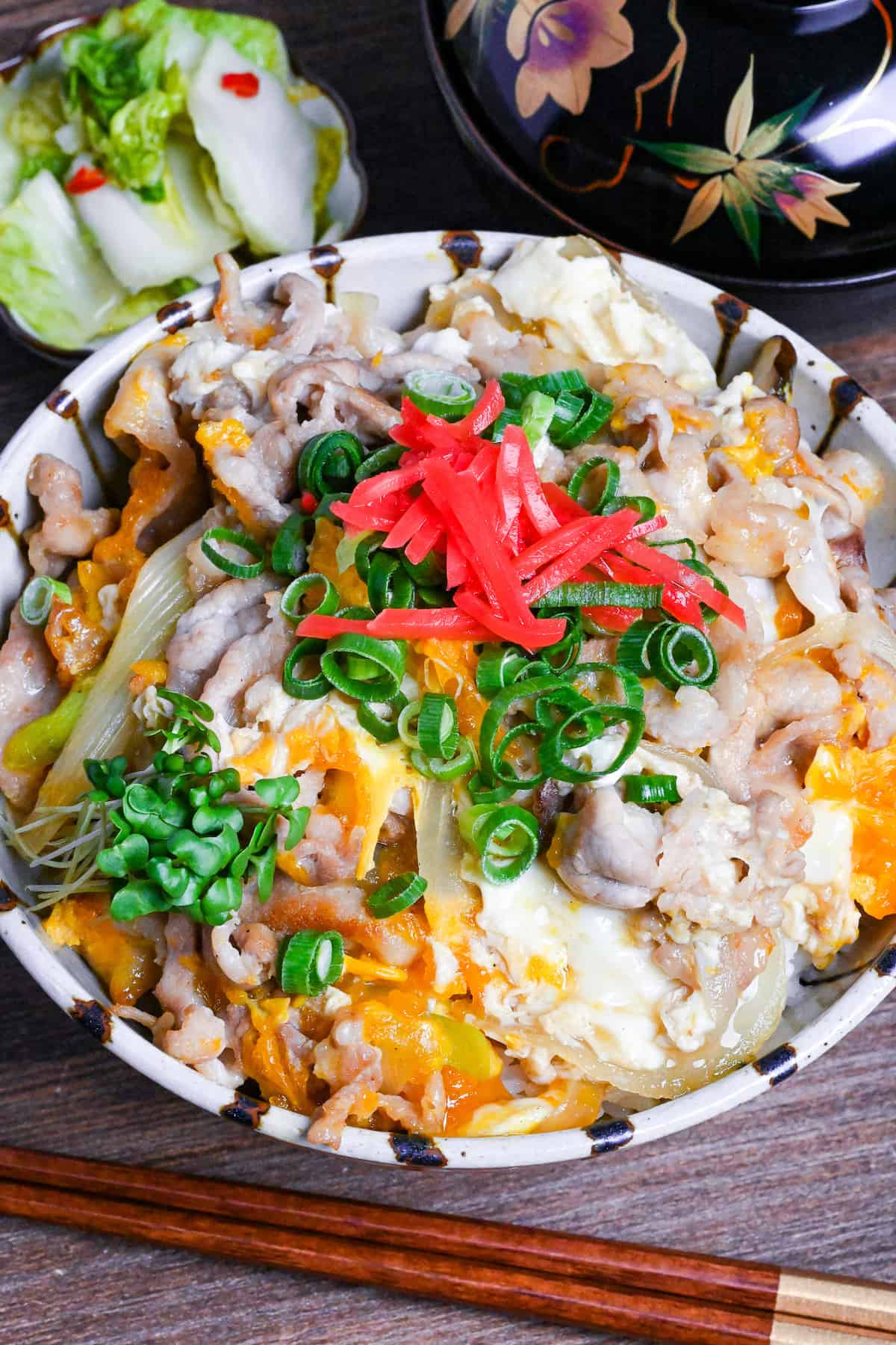 Tanin Don (Japanese pork and egg rice bowl) in a striped bowl topped with red pickled ginger and chopped green onions