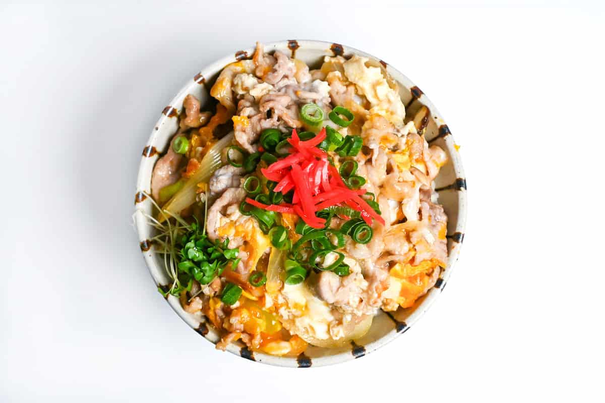 Tanin Don (Japanese pork and egg rice bowl) in a striped bowl topped with red pickled ginger and chopped green onions