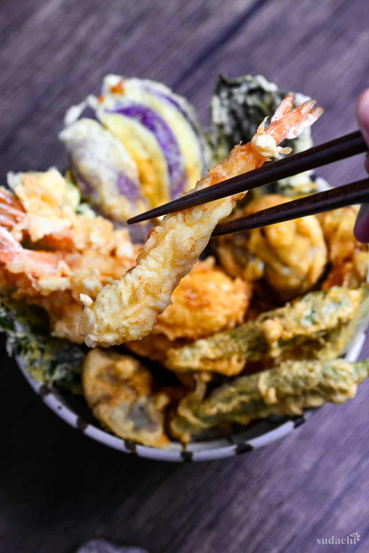 holding one tempura shrimp with chopsticks over a tempura rice bowl